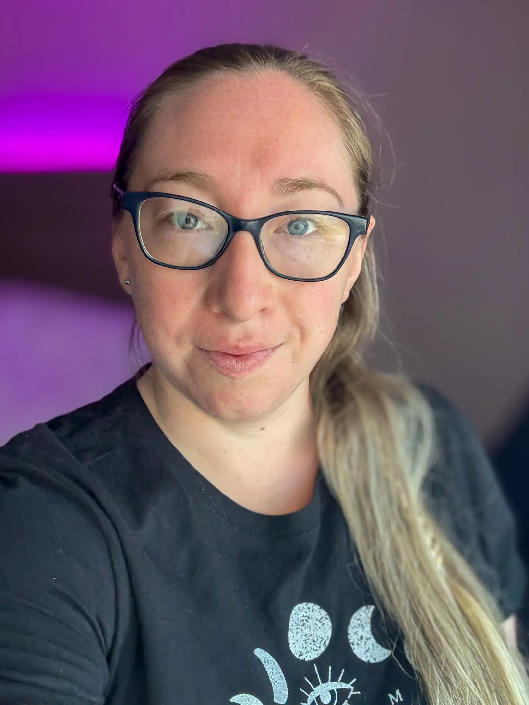 Blonde haired woman wearing glasses and a black t-shirt smiles. This woman is Emma Easter the owner of Emma Easter Handcrafted.