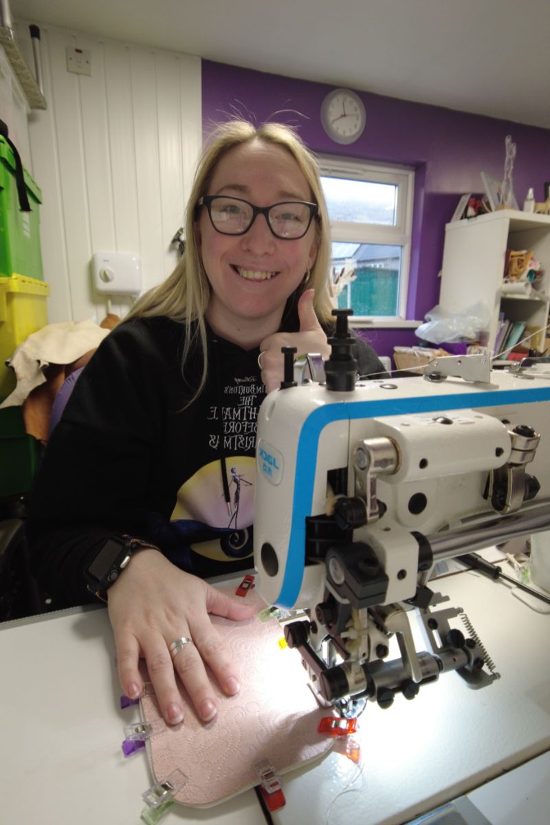 Emma Easter, artisan bag maker, smiling while handcrafting a leather bag at her sewing machine in her South East Wales studio.
