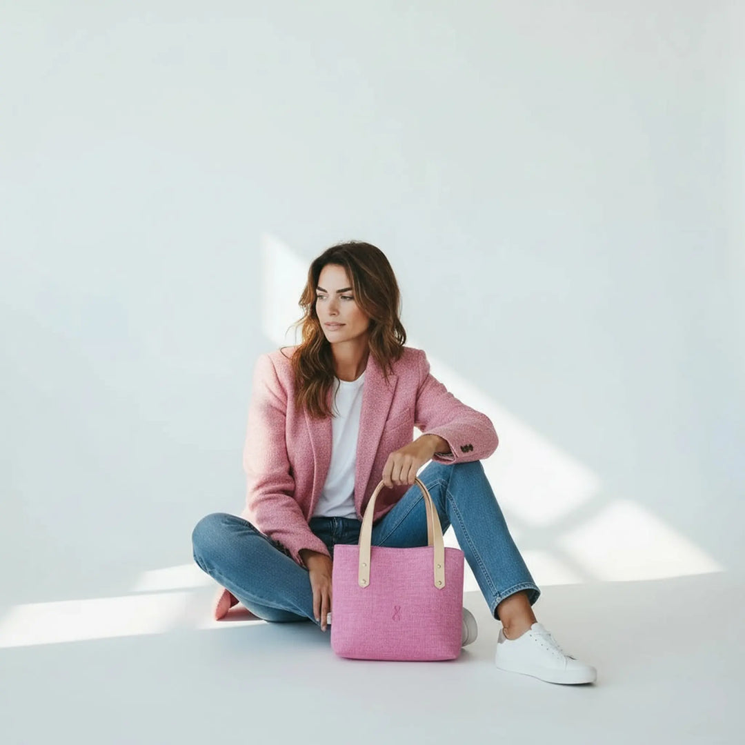 Woman sitting on the floor in a bright studio wearing a pink blazer and jeans, with a pink Harris Tweed® tote bag in front of her
