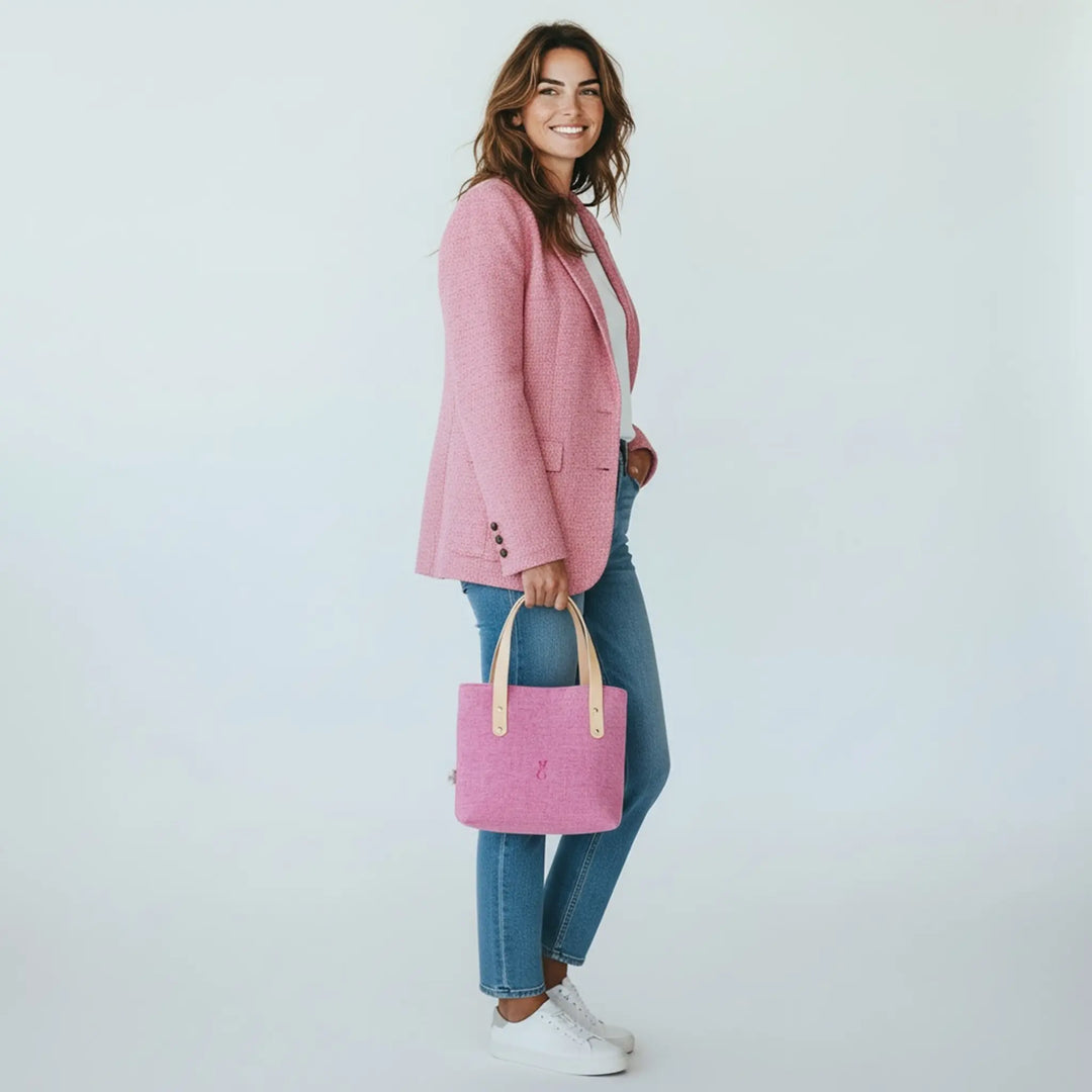 Woman standing in a white studio wearing jeans and a pink blazer, holding a pink Harris Tweed® tote bag by her side