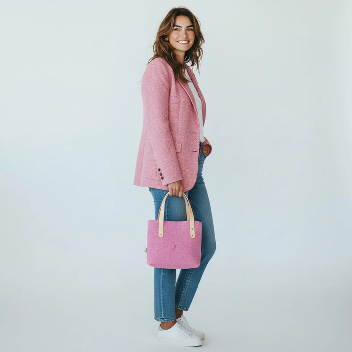 Woman standing in a white studio wearing jeans and a pink blazer, holding a pink Harris Tweed® tote bag by her side