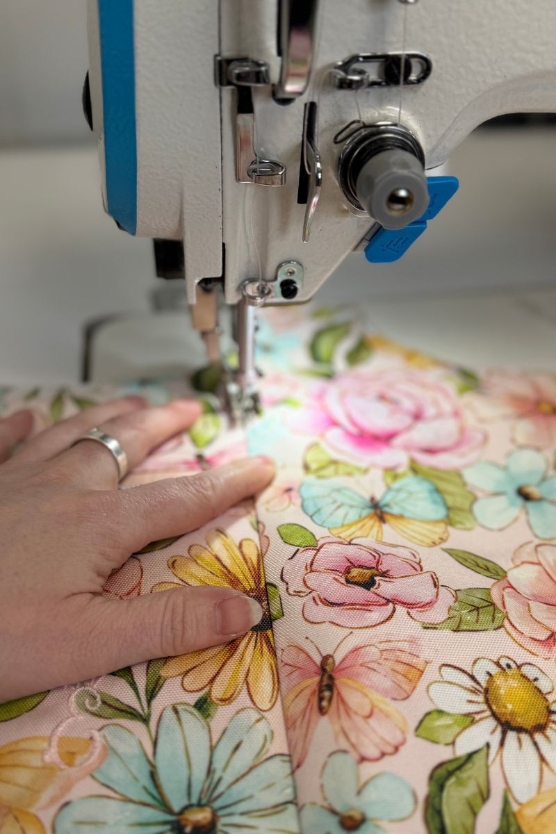 close up shot of Emma's left hand guiding the Penelope print fabric through the sewing machine