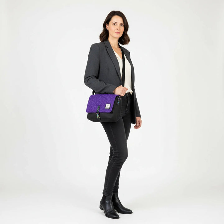 Woman in a white studio wearing a grey blazer, cream top & jeans, carrying a crossbody bag with a purple Harris Tweed® flap