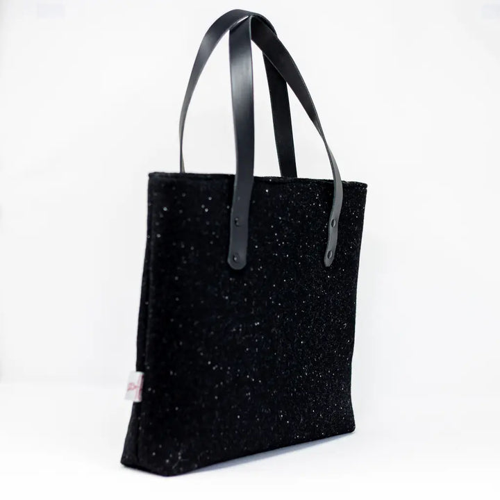 Angled side view of the black Harris Tweed tote bag with Harris Tweed label and black leather handles by Emma Easter Handcrafted.