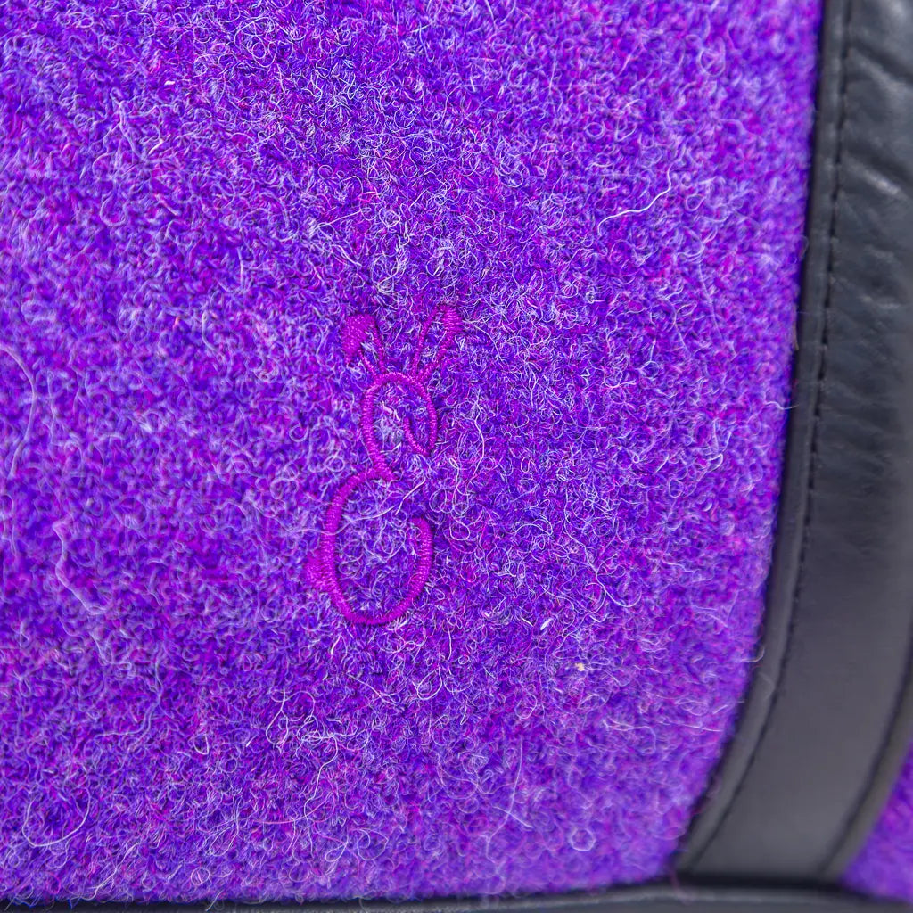 Close-up of the Bunny E logo on the purple Harris Tweed® cloth and black leather trim on the Rowena handbag by Emma Easter Handcrafted. 