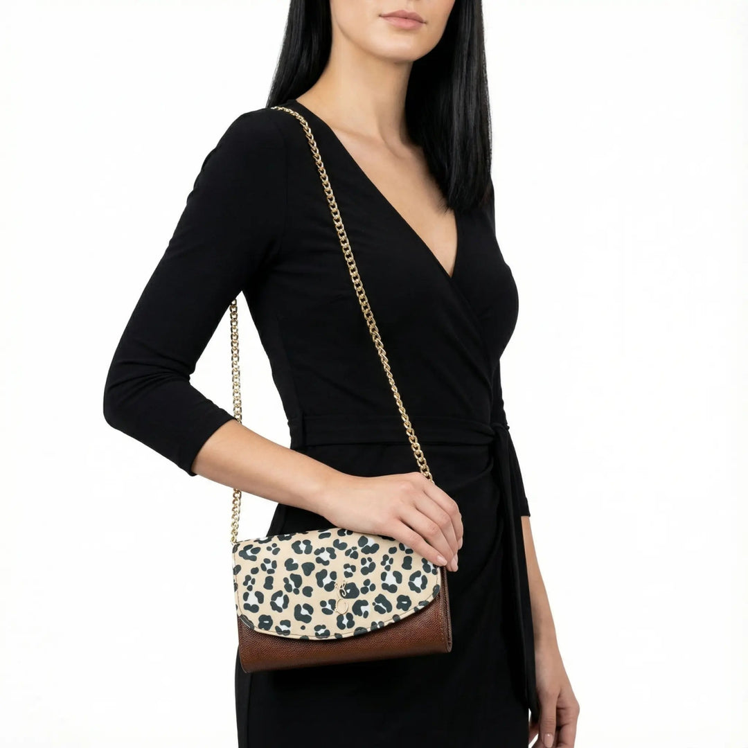 Woman in a black wrap dress holding the Leopard Italian Leather Handbag with a gold chain strap and leopard print flap, styled in a glamour pose against a clean white background.