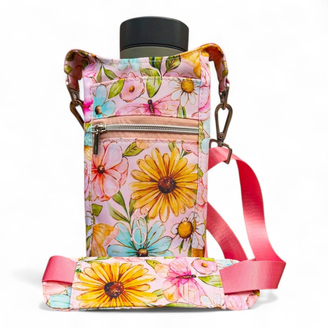 Penelope floral Bottle Buddy bag with pink strap, perfect for carrying drinks hands-free on hot days. Handmade in Wales with waterproof canvas and cheerful summery blooms.