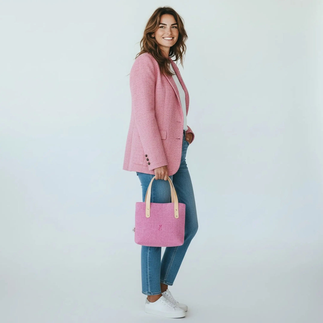 Woman standing in a white studio wearing jeans and a pink blazer, holding a pink Harris Tweed® tote bag by her side