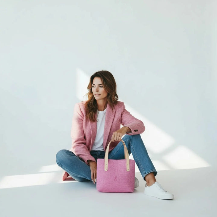 Woman sitting on the floor in a bright studio wearing a pink blazer and jeans, with a pink Harris Tweed® tote bag in front of her