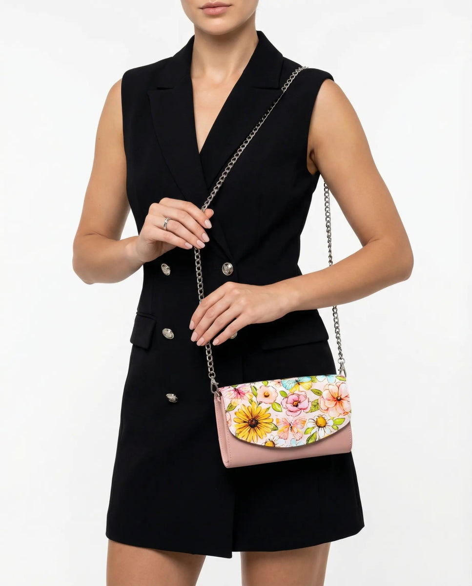 Woman presenting the Penelope Pink Italian Leather Handbag, featuring a floral flap and chain strap, styled in a sleeveless black blazer dress on a high-key white studio backdrop.