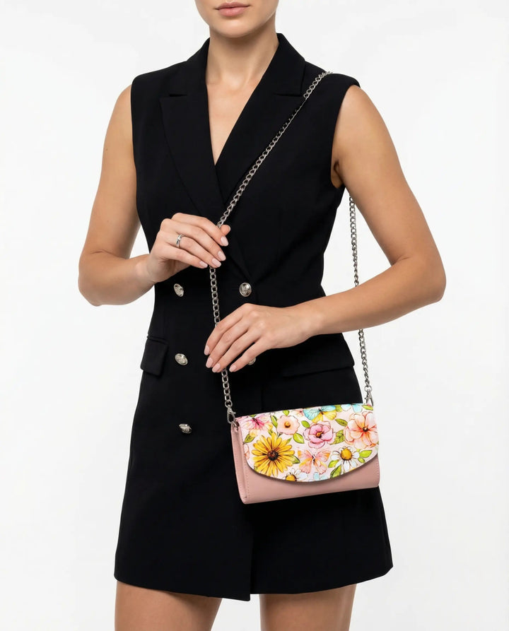 Woman presenting the Penelope Pink Italian Leather Handbag, featuring a floral flap and chain strap, styled in a sleeveless black blazer dress on a high-key white studio backdrop.