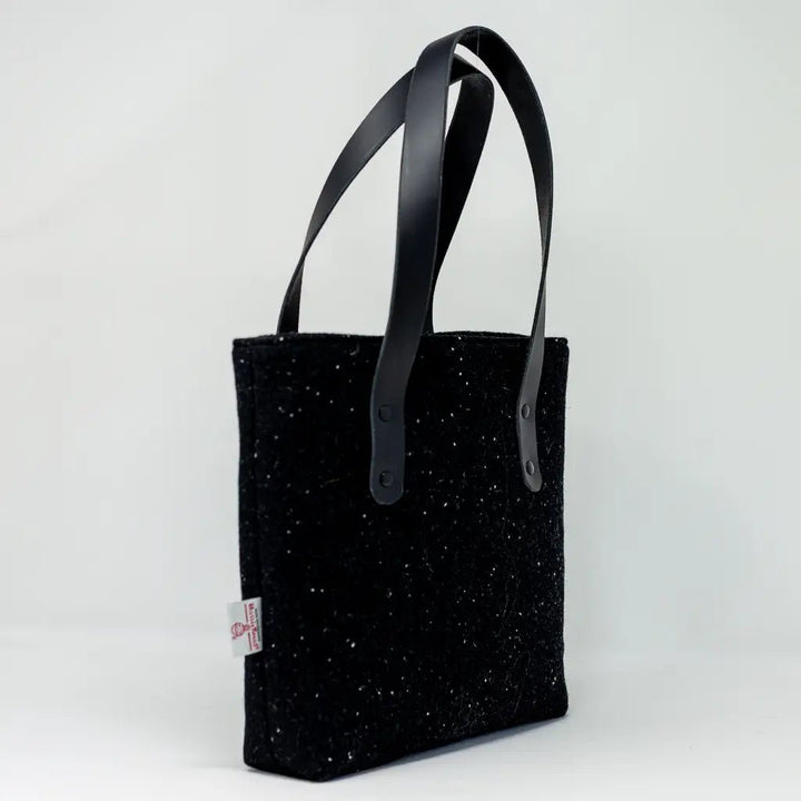 Side profile of the black Harris Tweed tote bag with leather handles and Harris Tweed certification label by Emma Easter Handcrafted.