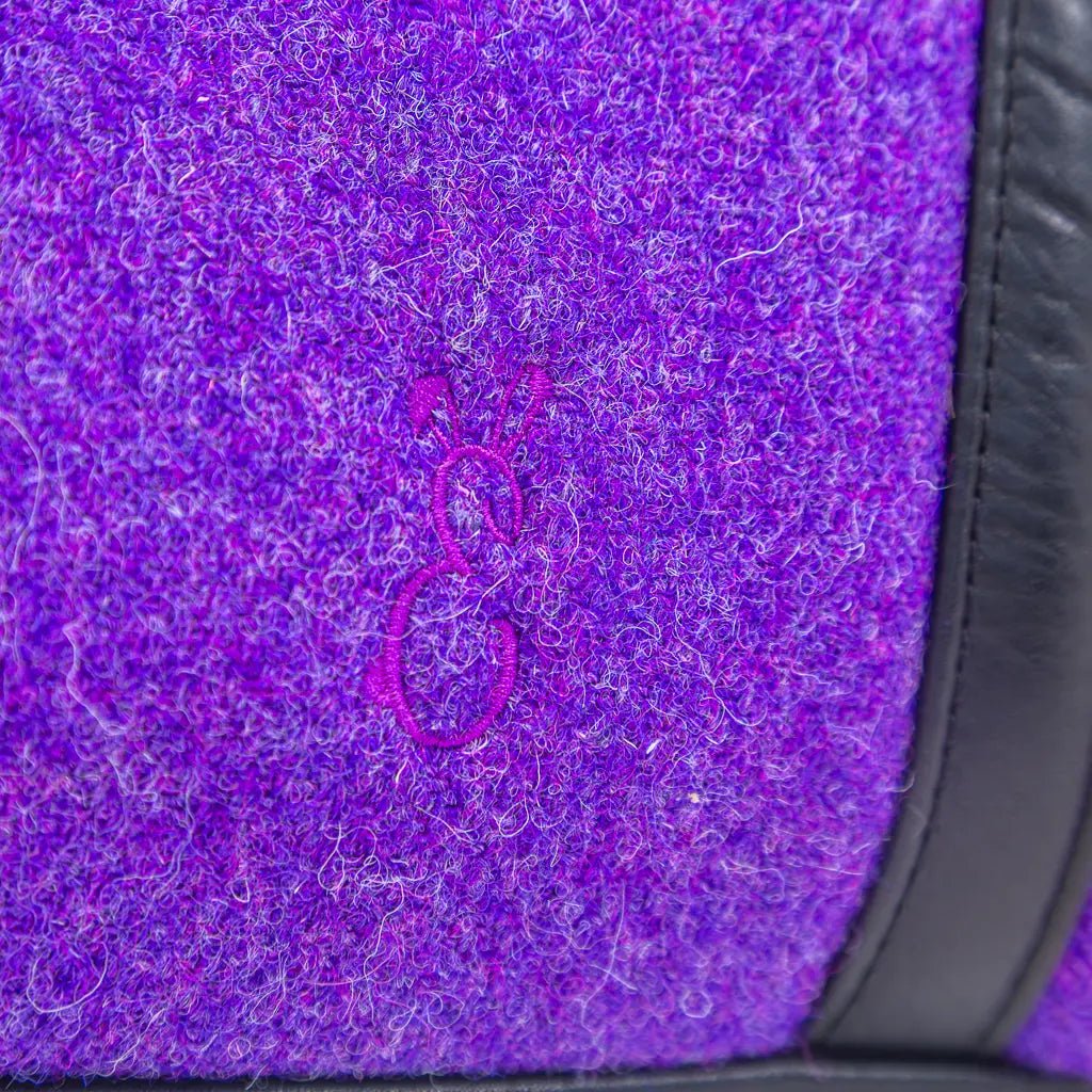 Close-up of the Bunny E logo on the purple Harris Tweed® cloth and black leather trim on the Rowena handbag by Emma Easter Handcrafted. 
