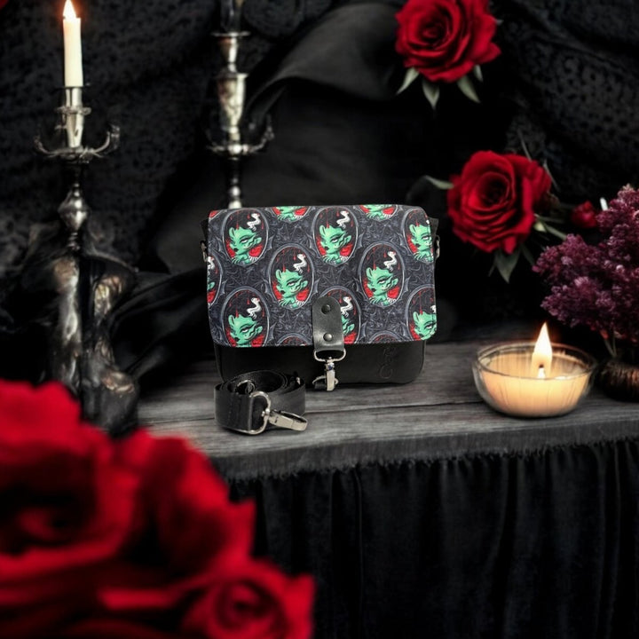 Gothic-themed artisan crossbody bag with a bold zombie portrait print, staged among black lace, red roses, and candlelight for a dark romantic aesthetic.