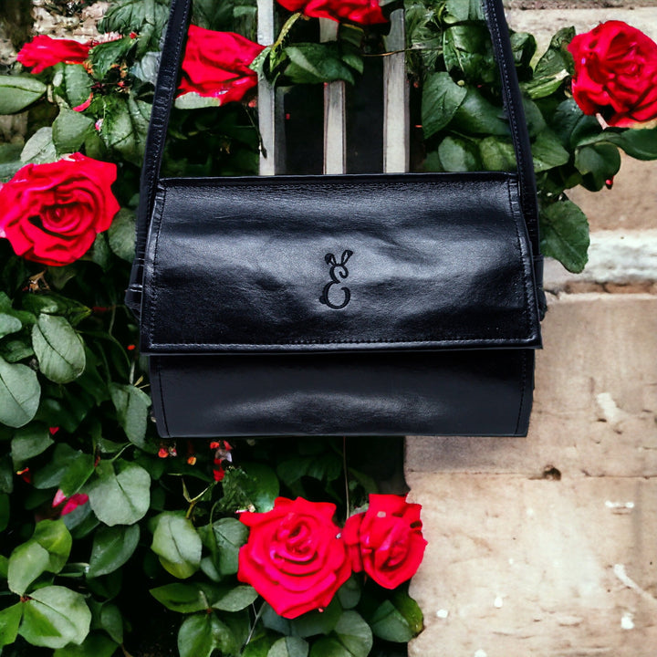the black rosa janine cross body bag hanging amongst red roses in a garden