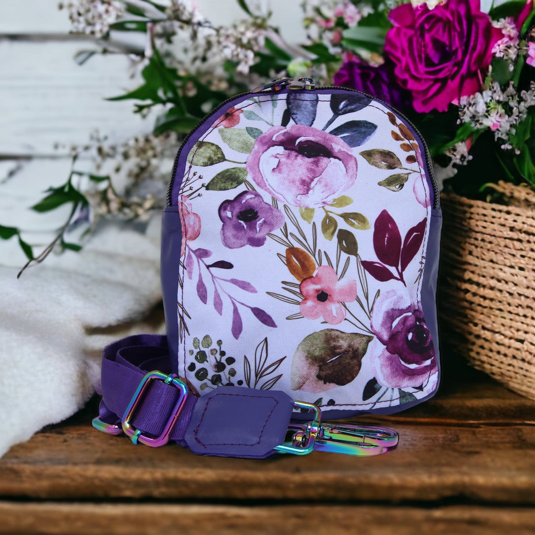 Purple Floral Mini Sling Bag on wooden shelf with floral arrangement to the right - Emma Easter Handcrafted